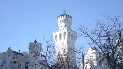 Revealing-the-snow-covered-mountains-behind-the-Neuschwanstein-Castle-towers-under-a-cloudless,-cold-blue-sky