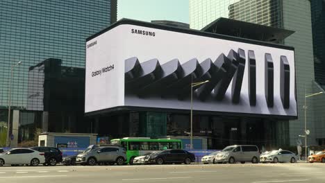 Advertisement-of-Samsung-Galaxy-Watch-Four-on-Largest-Outdoor-Digital-Billboard-Curved-Display-on-SMTown-Media-Facade-in-WTC-Gangnam-District-of-Seoul,-cars-in-a-traffic-jam
