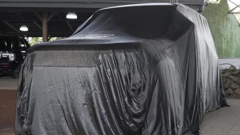 Land-rover-Defender-new-generation,-British-off-road-car,-covered-with-black-tarpaulin-to-give-surprise