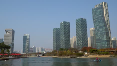 Safeguard-person-driving-water-ski-on-a-lake-in-Songdo-Central-Park-with-modern-futuristic-skyscrapers-and-Incheon-urban-skyline-in-Autumn---establishing-wide-shot