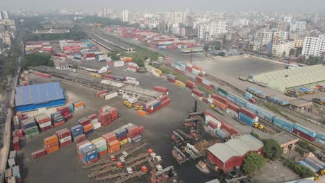 Aerial-drone-flyover-inland-shipping-container-depot-in-a-city,-daylight