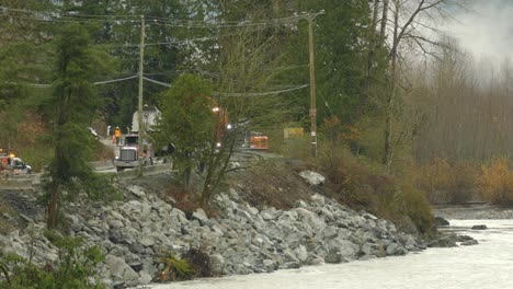 Eine-Entfernte-Aufnahme-Eines-Bauteams,-Das-Eine-Beschädigte-Straße-Und-Ein-Flussufer-Repariert,-Die-Durch-Die-Verheerenden-Überschwemmungen-In-Abbotsford-Verursacht-Wurden,-Während-Ein-Muldenkipper-Steine-An-Einen-Bagger-In-British-Columbia,-Kanada,-Ablädt