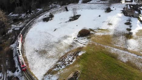 Luftaufnahme:-Rot-weißer-Zug-In-Den-Alpen,-Der-Durch-Eine-Kurve-Fährt-Und-Etwas-Schnee-Hat