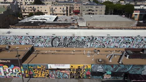 Aerial-view-away-from-a-wall-with-the-text-California-and-graffiti,-in-sunny-San-francisco,-USA---Pull-back,-drone-shot