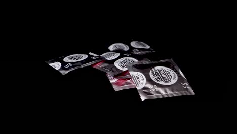 Silberne-Kondompackungen-Werden-In-Zeitlupe-Auf-Schwarze-Oberfläche-Geworfen