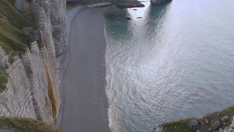 Top-down-shot-of-empty-pebbly-etretat-beach-with-calm-ocean-shore-and-cliffs