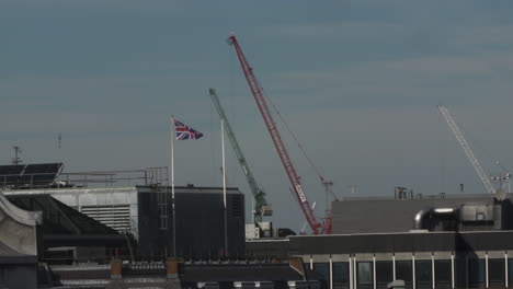 Rooftop-View-Of-Construction-Cranes-Moving-And-Union-Jack-On-Flagpole-In-London