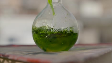 Slow-motion-colourful-green-liquid-solution-pouring-into-spherical-glass-flask-outside-closeup