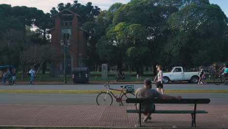 Cyclist-sits-on-bench-watching-people-walk-by