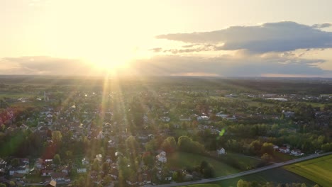 Bright-sunny-evening-after-a-beautiful-spring-day,-flying-backward-with-a-drone-showing-a-little-town-under-sunshine-with-some-clouds-in-the-sky