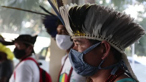 Indigenous-man-from-a-tribe-in-the-Amazon-rainforest-at-a-protest-wearing-a-traditional-feather-headdress-and-a-protective-face-mask