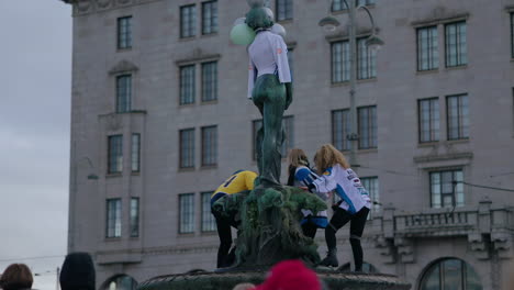 Young-women-wearing-national-team-jerseys,-standing-on-a-fountain-celebrating-Ice-hockey-gold-medal,-in-Helsinki,-Finland