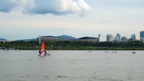 Windsurfer-Und-Paddle-Boarding-Im-Han-Fluss-Mit-Jamsil-Olympiastadion-Im-Hintergrund-In-Seoul,-Südkorea