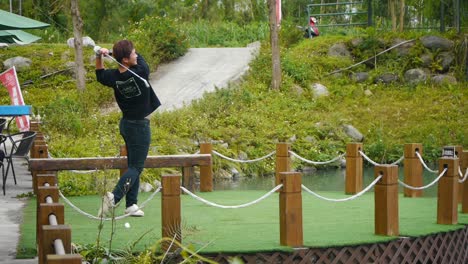 Asian-man-swings-golf-club-and-smacks-golf-ball-off-golfing-platform