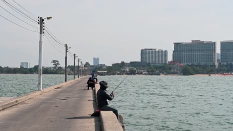A-man-with-a-hoodie-casting-its-lure-into-the-water-then-reels-in,-Pattaya-Fishing-Dock,-Chonburi,-Thailand