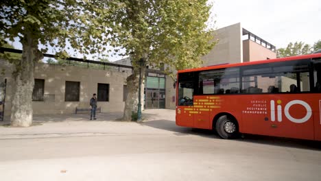 Roter-Bus-Regional-Occitanie-Transport-Lio-Kommt-An-Bushaltestelle-Mit-Wartenden-Leuten-An,-Schwenk-Nach-Links,-Folgeaufnahme