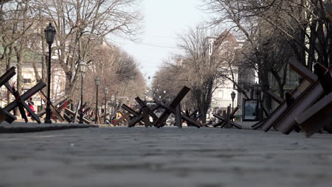 People-walk-past-tank-traps-made-from-welded-steel-metal-girders-on-a-cobbled-street-during-the-Russian-invasion-of-Ukraine