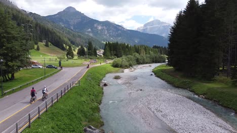 Val-Di-Fassa-Im-Trentino,-Dolomiten,-Italien---Drohnenaufnahme-Von-Radtouristen,-Blauem-Fluss-Und-Grünem-Gebirgstal