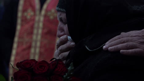 An-elderly-woman-wearing-black-weeps-into-a-handkerchief-held-to-her-mouth-while-holding-dark-red-roses-at-a-funeral-of-a-fallen-Ukraine-Soldier-during-the-Russian-invasion-of-the-country