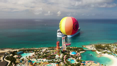 Rotierende-Luftaufnahme-Des-Heißluftballons-Im-Vordergrund-Auf-Cococay-Island-Mit-Wasserrutschen-Und-Einem-Kreuzfahrtschiff-Der-Royal-Caribbean-Im-Hintergrund