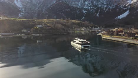 Passagierkatamaran-Vision-Der-Fjorde,-Die-Sich-Dem-Hafen-Von-Flam-Bei-Wunderschönem-Morgensonnenaufgang-Nähern-–-Verfolgung-Aus-Der-Luft-Und-Überfahrt-Hinter-Dem-Boot-Mit-Sonnenstrahlen-Und-Reflexionen,-Die-Auf-Katamaran-Und-Meer-Treffen