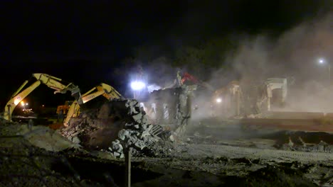 Bulldozers-working-at-night-removing-digging-asphalt-and-spreading-dust-on-the-strong-white-lights-of-the-highway-in-the-city,-cinematic-dark-gothic-scene