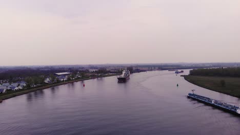 Aerial-View-of-Fortune-Cargo-Ship-Approaching-River-Bend-Along-Oude-Maas-On-Cloudy-Day-Passing-Another-Ship