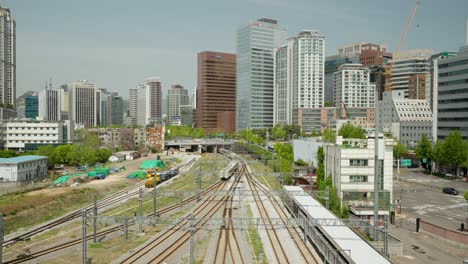 Tren-Que-Sale-Del-Depósito-De-La-Estación-De-Seúl-Con-Edificios-De-Gran-Altura-En-El-Fondo,-Corea-Del-Sur