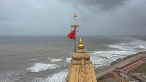 Aerial-shot-of-head-of-Somnath-mandir-with-Hindu-flag-blowing-in-the-windy-foggy-weather