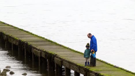 Father-holding-seaside-bucket-exploring-low-tide-UK-beach-boardwalk-with-his-son