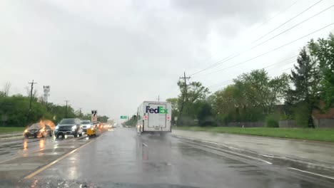 FedEx-Ground-truck-drives-by-on-a-rainy-day,-taking-off-at-stop-light