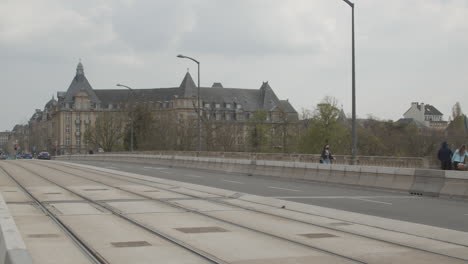 Frau-Mit-Gesichtsmaske-Geht-über-Die-Adolphe-Brücke-Mit-Der-Altstadt-Von-Luxemburg-Im-Hintergrund