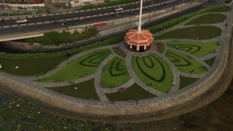 Park-designed-with-Lotus-flower-pattern,-Saigon-River,-traffic-bridge,-canal-and-main-road-drone-shot-orbiting-central-flagpole