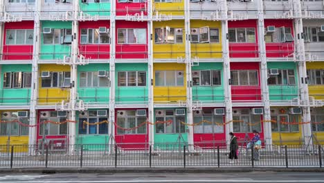 Pedestrians-are-seen-walking-past-a-colorful-facade-from-a-public-housing-building-in-Sham-Shui-Po,-Hong-Kong
