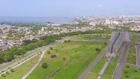 Aerial-forward-over-park-around-Faro-Colon-and-city-in-background,-Santo-Domingo