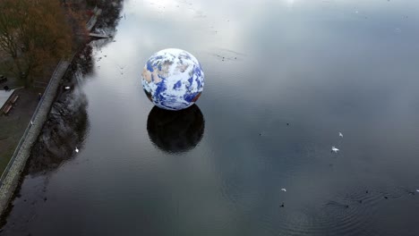 Luke-Jarram-floating-planet-earth-art-exhibit-aerial-view-at-Pennington-flash-lake-rising-dolly-left