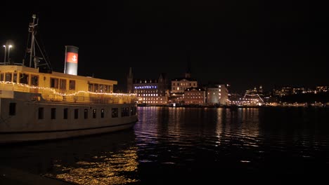 Statische-Ansicht-Eines-Wunderschön-Dekorierten-Dampfschiffs,-Das-Nachts-Am-Flussufer-Anlegt,-Mit-Blick-Auf-Die-Stadt-Im-Hintergrund-Im-Zentrum-Von-Stockholm,-Schweden