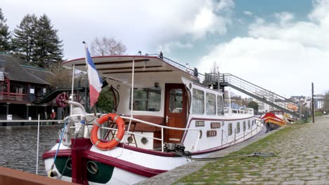 A-fixed-shot-of-a-narrowboat,-docked-in-the-Erdre-river-in-Nantes-with-a-French-flag-on-the-back