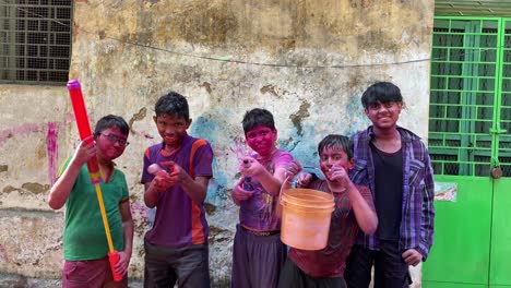 Group-of-Cheerful-kids-with-color-bucket,-pichkari-shouting-at-camera-after-playing-with-colorful-Holi-powder-during-festival-celebration