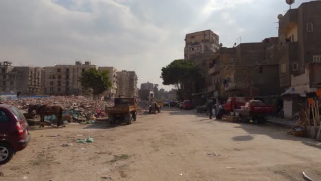Condiciones-De-Vida-Muy-Malas-En-Una-Parte-Pobre-De-La-Ciudad-De-El-Cairo,-Tráfico-En-Un-Camino-Arenoso