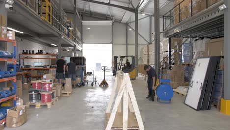 Workers-at-a-solar-panel-installation-warehouse-loading-crates-and-preparing-shipments,-Dolly-right-reveal-shot