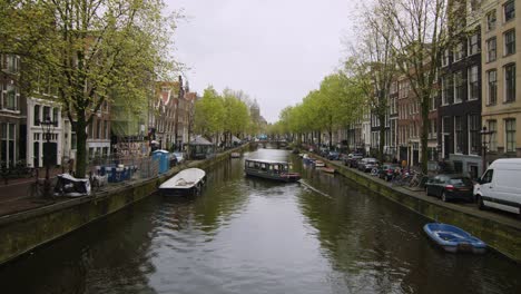 Old-city-Amsterdam-canal-on-spring-cloudy-day-with-docking-boats,-wide-static-shot,-Holland