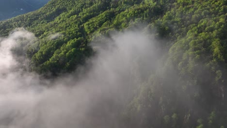 Flight-through-grey-clouds-along-steep-lush-Italian-alp-hillside