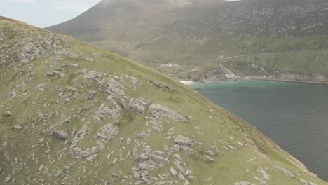 Drone-Flying-Over-Foliage-covered-Hill-Revealing-White-Sand-Keem-Beach-On-The-Atlantic-Ocean-Coast-In-Achill-Island,-County-Mayo,-Ireland