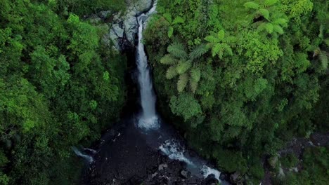 Aerial-view-from-drone-flying-over-nature-view-a-river-that-ends-in-a-waterfall-with-surrounding-vegetation
