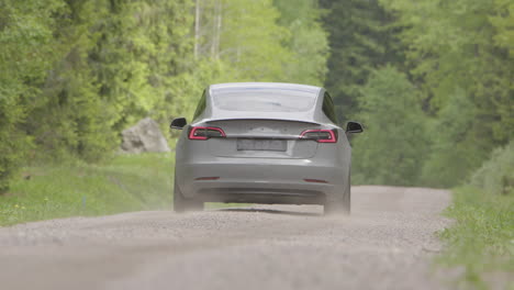 Langes-Objektiv-Hinten-–-Ein-2020-Tesla-Model-3-Fährt-Eine-Bewaldete-Unbefestigte-Straße-Entlang