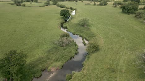An-aerial-view-of-the-tiny-river-Arrow-as-it-twists-it's-way-through-the-Warwickshire-countryside,-England