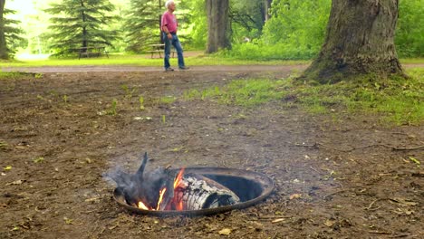 Man-walks-from-left-to-right-in-the-background-of-a-campsite-fire
