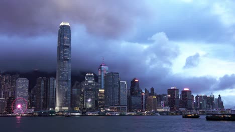 Eine-Stationäre-Weitwinkelaufnahme-Eines-Passagiertransportschiffs-Der-Star-Ferry,-Während-Es-An-Einem-Bewölkten-Tag-Im-Victoria-Harbour-Entlang-Der-Gebäude-Und-Wolkenkratzer-In-Hongkong-Fährt