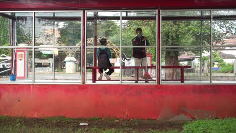 Student-sitting-on-bench-at-bus-station-while-clean-service-sweep-with-broom